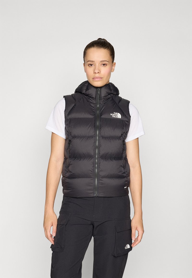 Zwarte puffervest met capuchon, rits aan de voorkant en elastische randen. Draagbaar over een wit shirt, met een klein logo op de linkerkant van de borst.