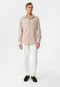 Lichtbeige lange mouwen shirt met een kraag en knopen, gecombineerd met witte broek, met donkere schoenen, staand tegen een neutrale achtergrond.