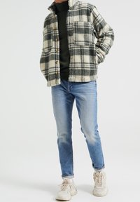 Ruudullinen fleecetakki kerman ja harmaan sävyissä, jossa on nappisuljenta edessä, kaksi sivutaskua, yhdistetty vaaleansinisten farkkujen ja beigen väristen tennarien kanssa.