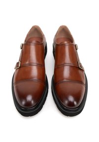 Bruine lederen schoenen met een gladde textuur, voorzien van twee gespen en een contrasterende zwarte rubberen zool. Ronde neus en gestikte details.