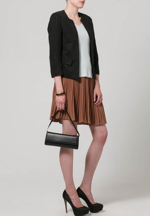 Zwarte getailleerde blazer, lichtblauwe ribbeltrui, geplooide beige rok, zwarte hoge hakken en een zwarte clutch.