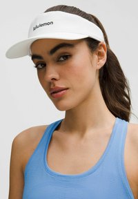 Balta vizorinė kepurė su tekstūruotu diržu ir "lululemon" logotipu priekyje, derinama su šviesiai mėlynu sportiniu tank topu.