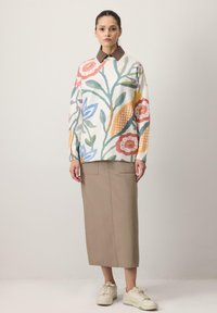 Suéter de punto con patrón floral multicolor, escote redondo, mangas largas. Combinado con una falda beige hasta la rodilla y zapatillas blancas.