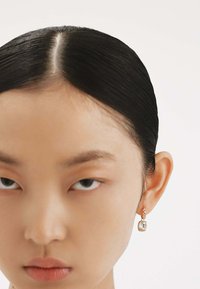 Pendientes de plata en forma de aretes con un colgante de cristal rectangular y un pequeño acento de perla, sobre un fondo claro.