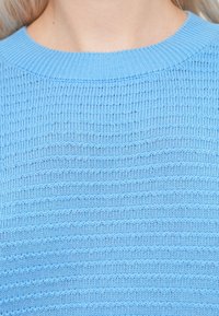 Pull en maille bleu clair avec un motif texturé et un col ras du cou côtelé. Tissu doux et respirant avec un design décontracté.