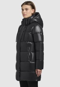 Sort puffer-jakke med en blank finish, der har hætte, lynlåslommer og en kviltet design. Jakken har en mellemlang pasform og snoretræk detaljer.