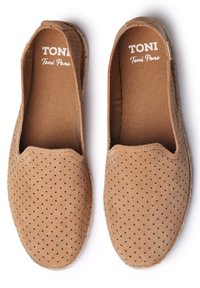 Zapatos slip-on perforados en color marrón claro, con una suave textura de ante, puntera redondeada y borde cosido. El forro interior es de tela marrón con el logo.