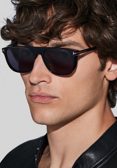 Ochelari de soare rectangulări negri cu lentile închise, având accente metalice și un logo de marcă distinctiv; design elegant al ramei.