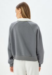 Grå sweatshirt med en krave i cremfarge, ribbede manchetter og kant, samt raglanærmer. Blødt materiale og en afslappet pasform.