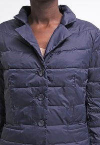 Námořnická pufrová bunda s límcem, zdobená prošívaným vzorem, čtyřmi knoflíky a dvěma předními kapsami. Hladká textura a elegantní design.