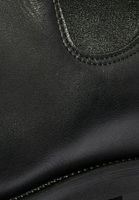 Czarna skórzana boot z gładkim wykończeniem, kontrastującą tkaniną w łatce i widocznym szwem wzdłuż krawędzi. Zaokrąglony kształt palców.