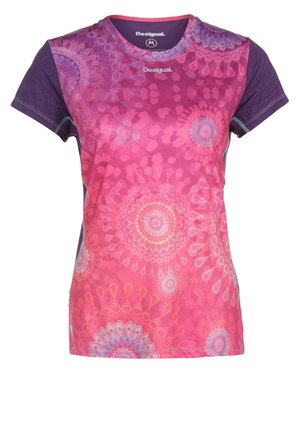 Femme portant un t-shirt de sport rose vif à motifs et des leggings roses unis avec des chaussures de course grises et turquoise, posant avec une jambe levée.