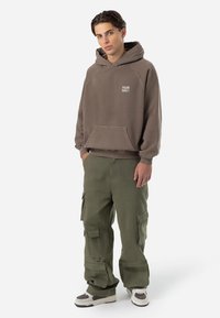 Felpa con cappuccio marrone, dotata di tasca frontale e logo, abbinata a pantaloni cargo verde oliva con molte tasche e una vestibilità comoda.