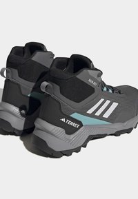 Scarpe da trekking nere e grigie con tomaia in mesh, accenti testurizzati, dettagli blu e una suola in gomma spessa progettata per la trazione.