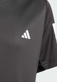 Schwarzes Sport-T-Shirt aus glattem Stoff, mit einem weißen gestreiften Logo im linken Brustbereich und kurzen Ärmeln.