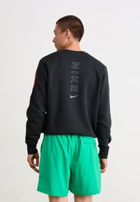 Sort sweatshirt med "NIKE" tekst på ryggen, parret med lysegrønne shorts med en sidelomme og elastisk talje.