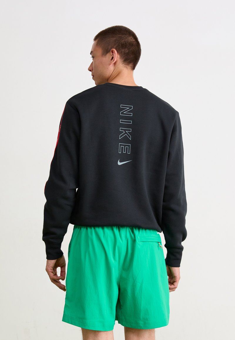 Sort sweatshirt med "NIKE" tekst på ryggen, parret med lysegrønne shorts med en sidelomme og elastisk talje.