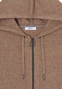 Sweat à capuche marron avec fermeture éclair, fabriqué en tissu doux, doté d'une fermeture éclair frontale avec un tire-zip circulaire et des cordons décoratifs. L'étiquette indique "CECIL".