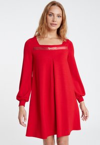 Rotes langärmliges Kleid mit quadratischem Ausschnitt, goldene Hardware-Akzent am Dekolleté, gefältetes Design und schmal zulaufende Manschetten. Weicher, glatter Stoff.