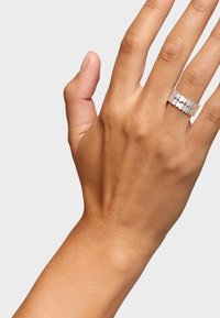 Anillo de plata con un patrón floral recortado, que presenta formas redondeadas interconectadas. Se lleva en una mano que muestra piel suave y un color de uñas natural.