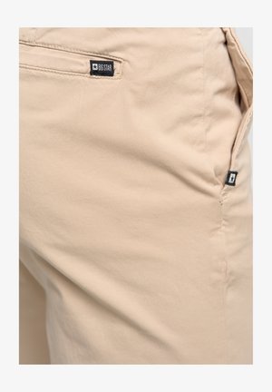 Pantaloni in cotone beige dal design semplice, con una tasca sul retro con un'etichetta "BIG STAR" e una texture liscia e leggermente stropicciata.