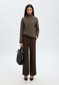 Rudas chevron raštas megztinis su aukštu kaklu, derinamas su plačiomis rudomis kelnėmis. Laiko juodą odinę rankinę ir dėvi smailiais juodais bateliais.