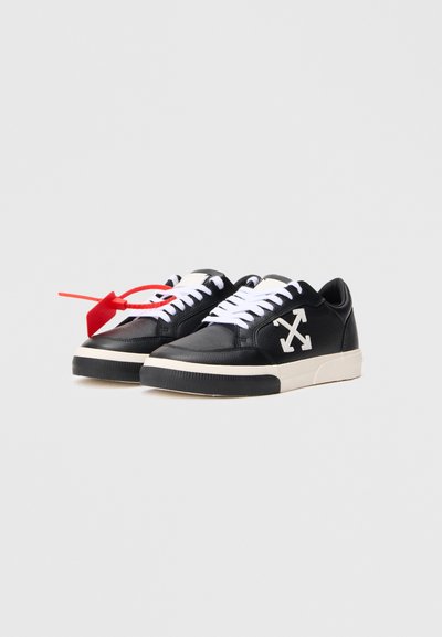 Sneakers in pelle nera con lacci bianchi e logo a forma di freccia. Presentano una tomaia testurizzata, suola in gomma e un'etichetta di accento rossa.