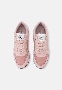 Zapatillas deportivas de color rosa claro con paneles de malla y ante, punta redonda, detalles blancos cerca del talón y suela de goma negra. Marca de piel de ternera en la lengüeta.