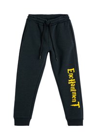 Pantalones de chándal negros con cinturilla elástica y cuerdas de ajuste, bolsillos laterales, tobillos con puños y texto vertical amarillo "Encanto" en la pierna izquierda.