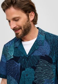 Korte mouw blouse in navy met abstracte turquoise en blauwe patronen. Voorzien van een puntkraag en zwarte knopen.