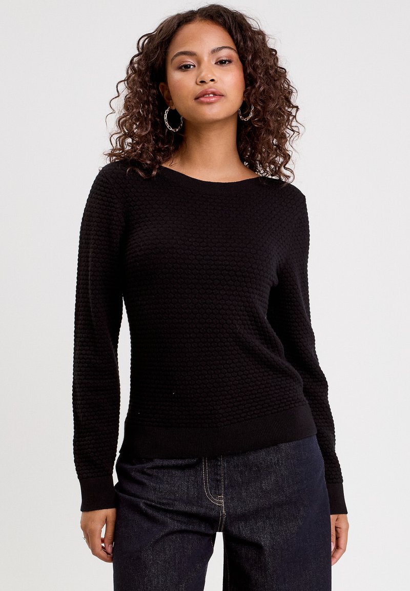 Pull en maille noir texturé avec des manches longues, un col rond et des poignets côtelés. Assorti avec un jean noir.