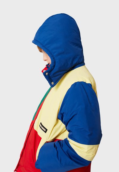 Giacca imbottita colorata in blu, giallo e rosso con cappuccio, dotata di chiusura con zip, bottoni a pressione e un'etichetta con logo sul lato.