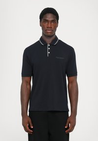 Marineblå polo-skjorte i bomull med en strukturert overflate, med en knappestolpe med to knapper, hvit krage og brodert logo på brystet.