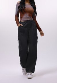 Pantalon cargo noir avec une ceinture élastique, des poches latérales et une coupe ample, associé à un haut à manches longues dégradé dans des tons bruns.