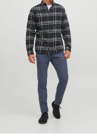 Camicia a flanella a quadri nera e grigia con maniche lunghe, chiusura a bottoni e colletto; abbinata a pantaloni blu texture e scarpe nere.
