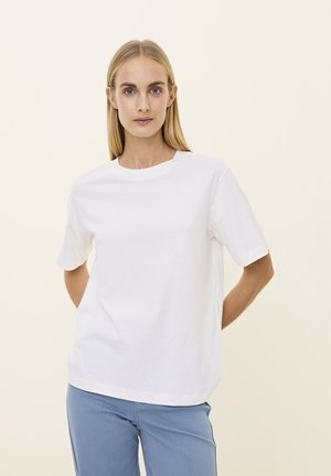 Witte katoen t-shirt met een ronde hals en korte mouwen. Eenvoudig ontwerp, ontspannen pasvorm. Draagt samen met lichtblauwe broek. Effen achtergrond.