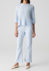 Pull en tricot bleu clair à manches trois-quarts avec ourlet côtelé. Associé à un jean évasé bleu clair et des ballerines couleur crème.