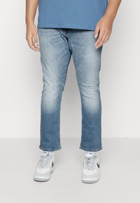 Jeans azul claro con un diseño desgastado, corte recto y ligero estiramiento. Combinados con zapatillas blancas con detalles y cordones grises.