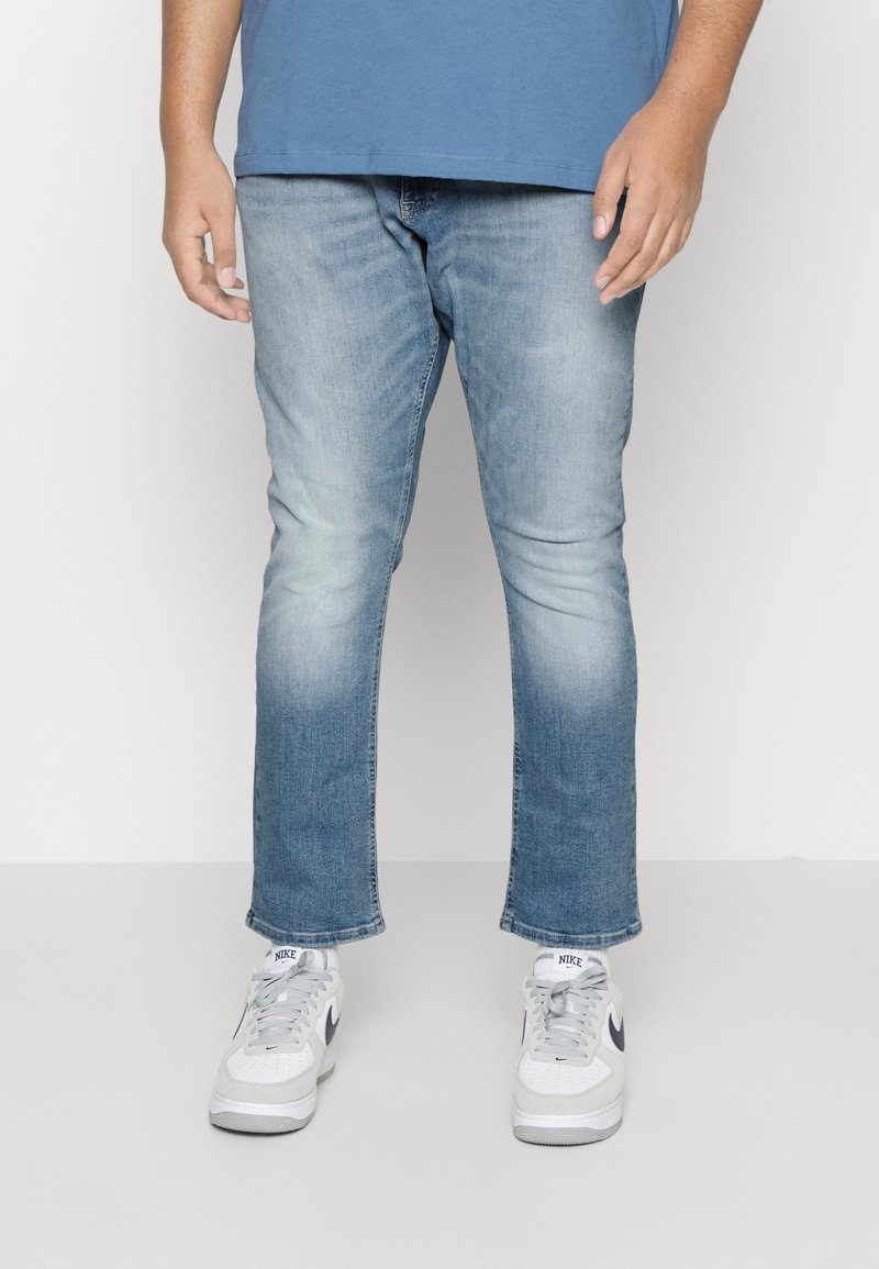 Jeans azul claro con un diseño desgastado, corte recto y ligero estiramiento. Combinados con zapatillas blancas con detalles y cordones grises.