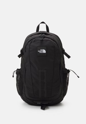 Black backpack made of durable fabric, featuring multiple compartments, adjustable straps, mesh side pockets, and a logo patch.