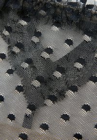 Zwarte tule stof met een hexagonale meshstructuur. Bevat gestructureerde stippen en een zachte, doorzichtige uitstraling. Gelaagde randafwerking.