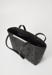 Geantă tote din piele neagră, cu un model împletit, deschisă în partea de sus, și două bretele pentru umăr. Interiorul este vizibil, cu un indiciu al unui fermoar argintiu.