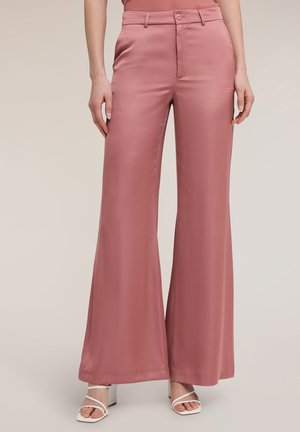 Femme portant un pantalon taille haute à jambes larges couleur rose poussière avec passants de ceinture et bouton de fermeture, assorti à des sandales blanches à talons blocs à brides.