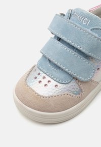 Lyseblå suede sneakers med to borrelåser, iriserende detaljer, rosa nagler, og beige suede-detaljer ved tåen og siden.