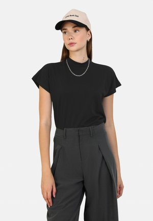 Top corto nero a maniche corte con collo alto, abbinato a pantaloni grigi su misura. Un cappello beige con testo e una collana in argento.