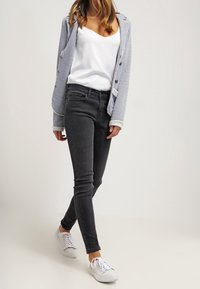 Grå jeans med en smal passform, med en slät yta, kombinerat med en vit linne och en mönstrad kavaj, avslutat med vita sneakers.