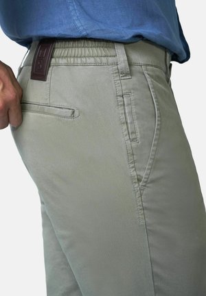 Mann trägt hellgraue Hose mit Gesäß- und Seitentaschen, zieht leicht an der Gesäßtasche, kombiniert mit einem blauen Hemd.