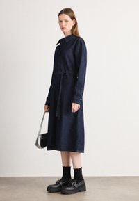 Mörk denimklänning med långa ärmar, knäppning framtill och bälte i midjan. Kombinerad med svarta platåskor och silverhandväska. Enkelt design, inga mönster.