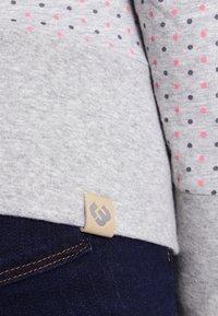 Grå sweatshirt med rosa och marinblå prickar, med en tygetikett på nederkant. I kombination med mörkblå denim med kontraststygn.