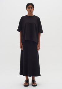 Čierny oversized top s krátkym rukávom v kombinácii s dlhou čiernou sukňou. Jednoduchý dizajn, hladká textura, doplnené o ploché čierne sandále.